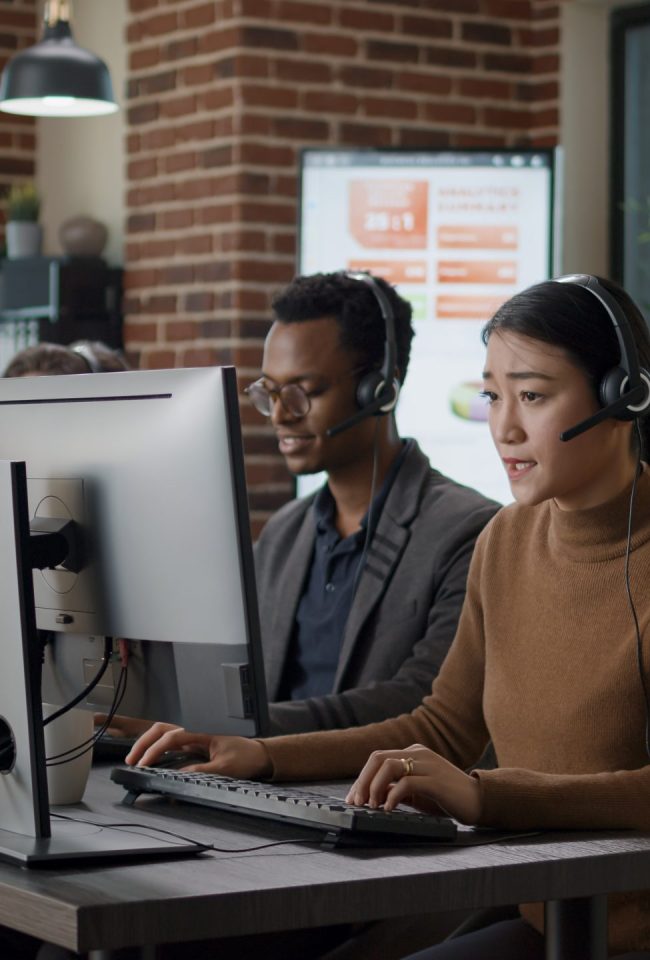 Multiethnic team of people working at call center office, using audio headset for telecommunications to help clients. People answering call on phone helpline, giving assistance at workstation.